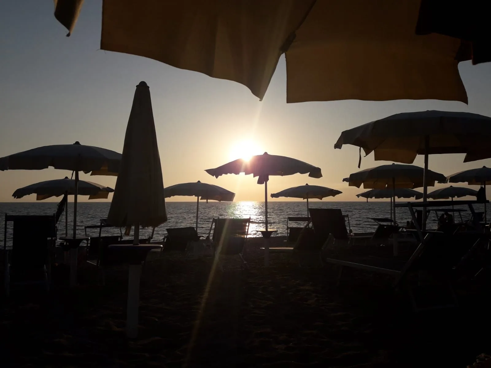 Tramonto sul golfo di Sant'Eufemia visto dalla spiaggia, con gli ombrelloni in controluce e il sole che si riflette sul mare