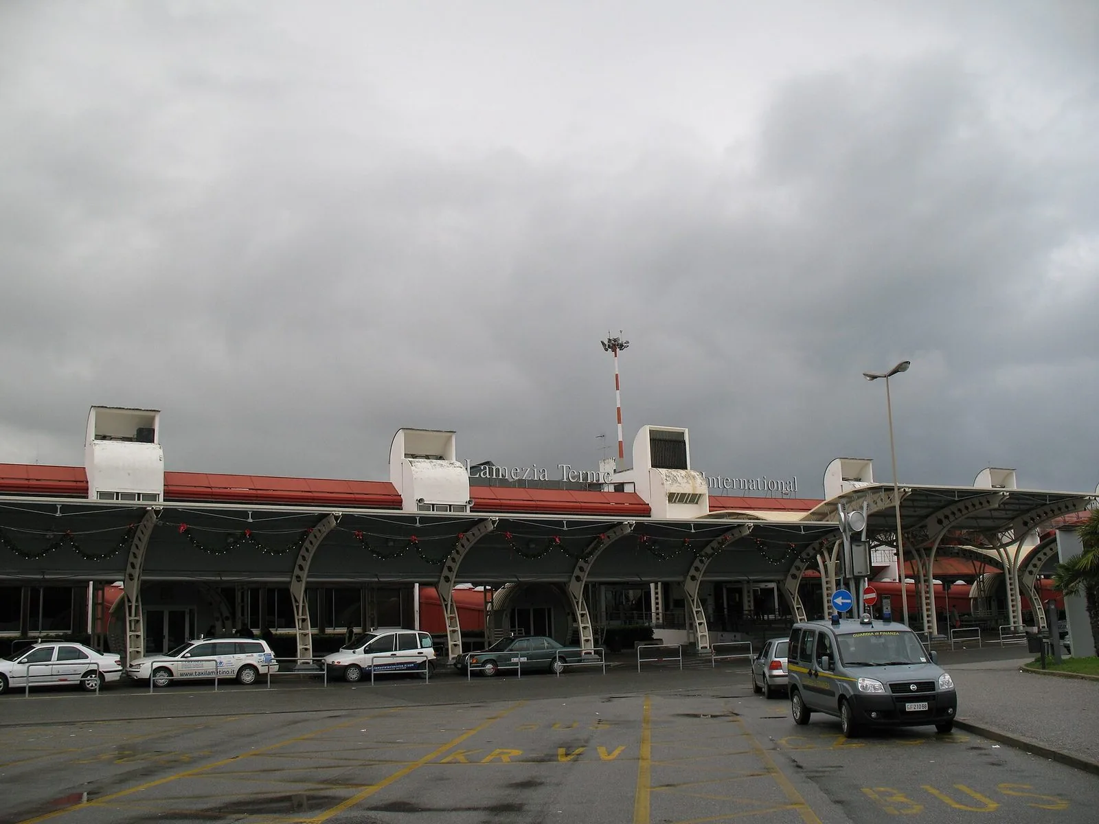 L'ingresso del terminal dell'aeroporto di Lamezia Terme con la pensilina ad archi, i taxi in sosta e il cielo nuvoloso