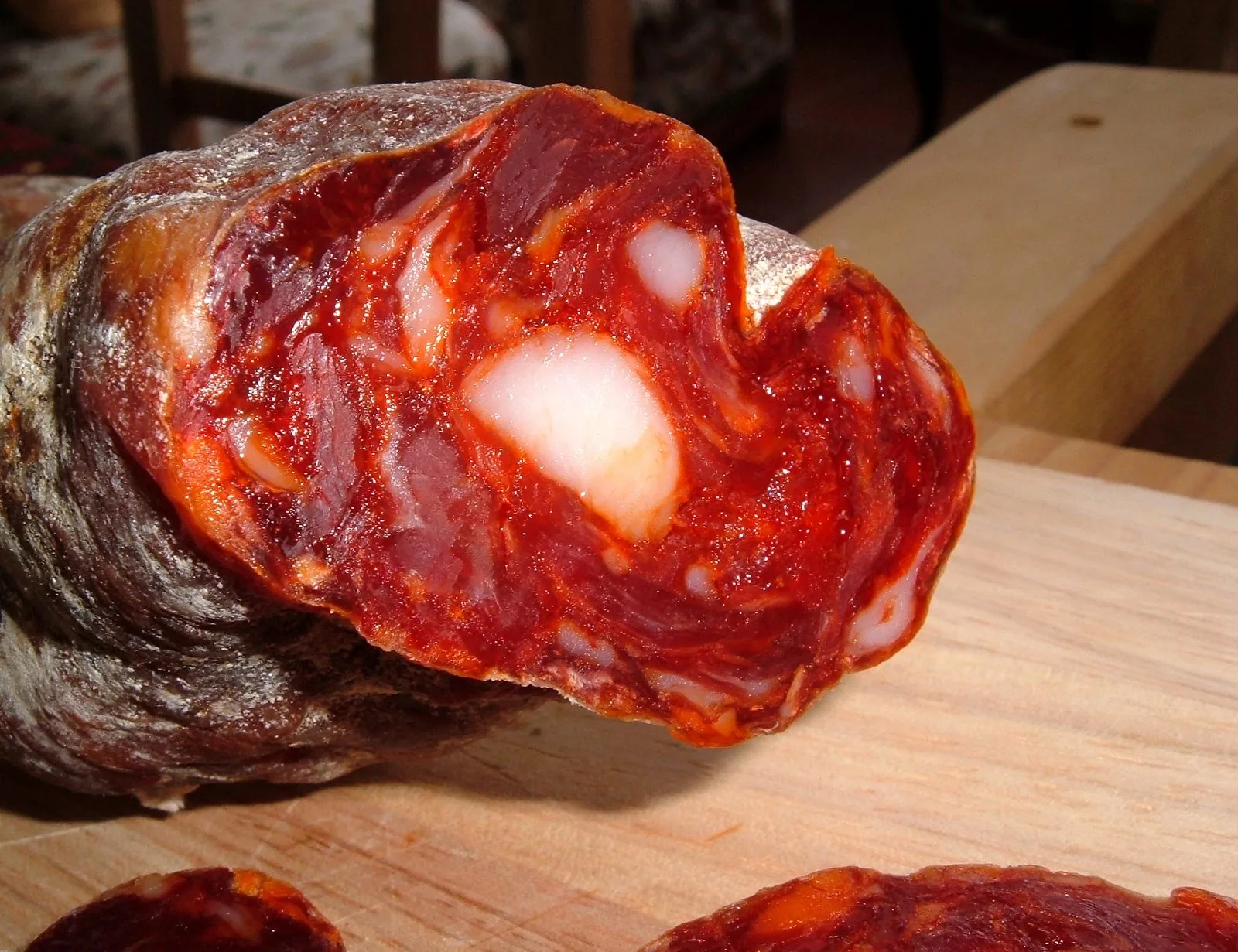 Una soppressata di Decollatura tagliata a metà, con la carne rossa di peperone e i pezzetti di grasso, su un tagliere di legno