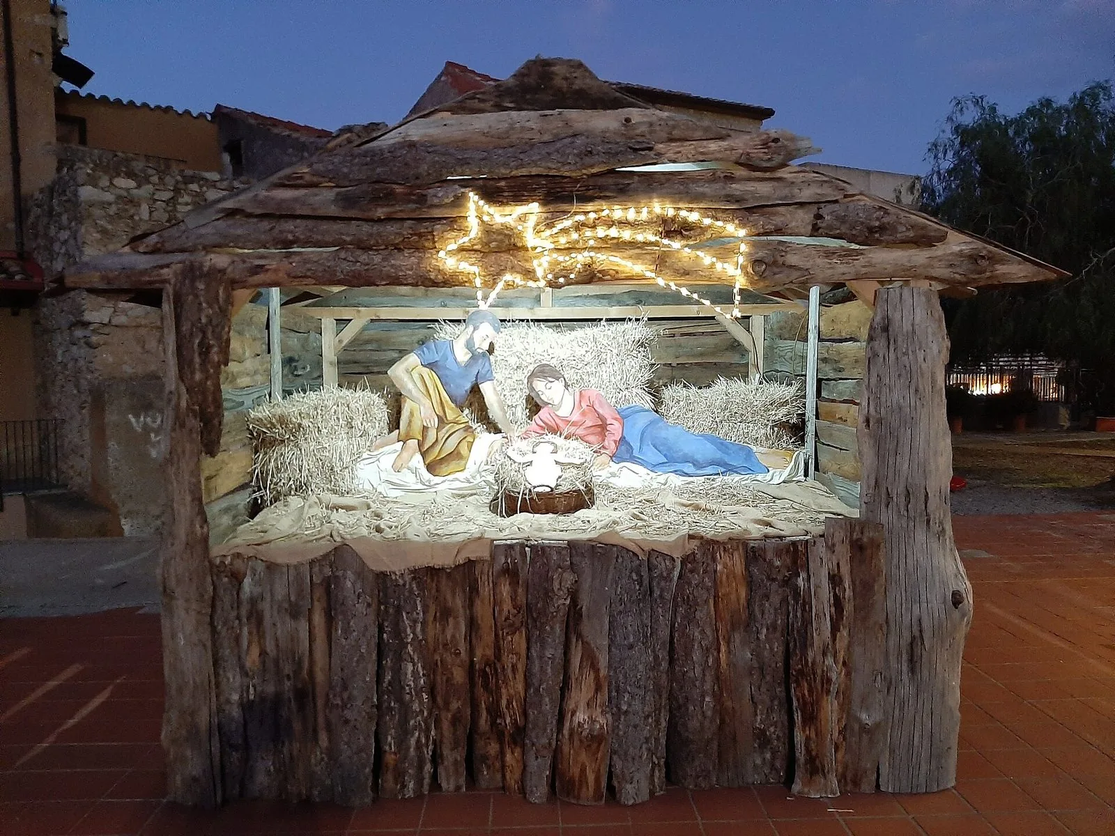 Un presepe in piazza a Badolato, con la Sacra Famiglia sotto una capanna di tronchi illuminata da una stella di luci